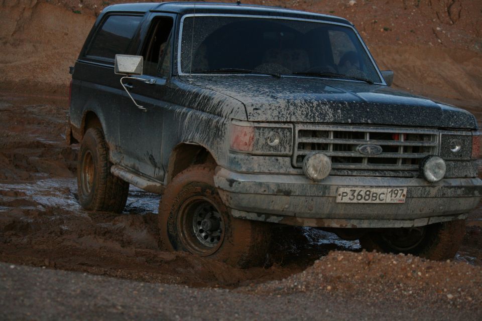 Dark 1987 Ford Bronco stuck in mud, 3q-front view