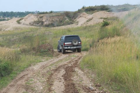1987 Ford Bronco - The Bronco navigates a rough, unpaved path in a rural, undeveloped landscape.