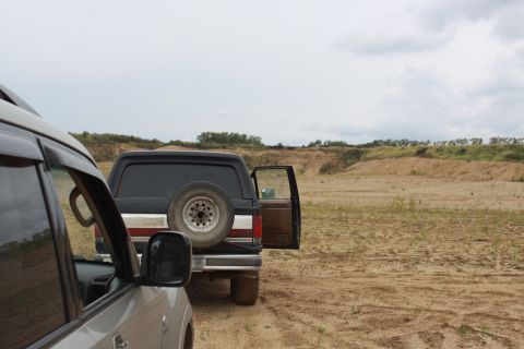 1987 Ford Bronco - A black SUV with a spare tire on its rear door is parked on a dirt road with its driver's side rear door open.