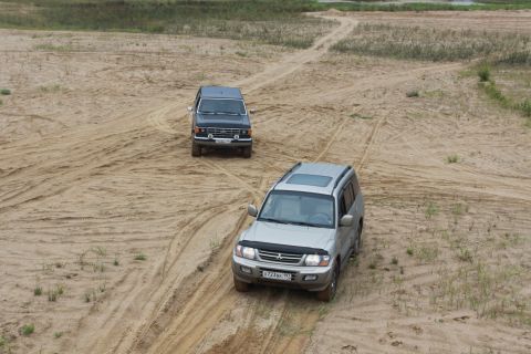 1987 Ford Bronco - Two SUVs navigate sandy terrain, kicking up dust as they drive.