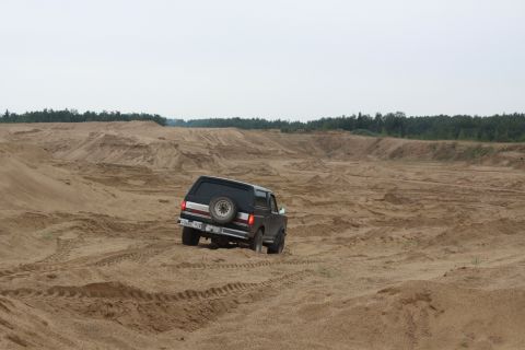 1987 Ford Bronco - A 1987 Ford Bronco navigates a sandy landscape under an overcast sky.