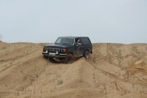 1987 Ford Bronco - A black 1987 Ford Bronco navigates sandy terrain under an overcast sky.