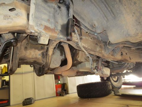 1996 Ford Bronco - Underside view of a vehicle's frame, suspension, and exhaust system, with a spare tire visible.