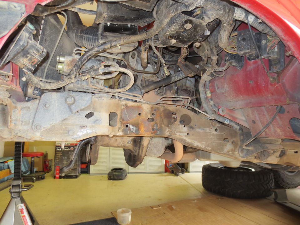 Red vehicle undercarriage with rusted frame, engine components, and exhaust system visible