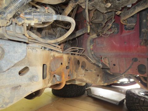 1996 Ford Bronco - Close-up view of a heavily rusted vehicle frame and engine bay wiring, with a red body panel in the background.