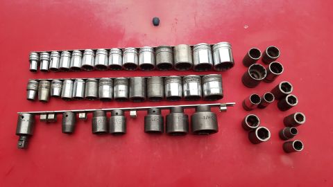 1965 Ford Mustang - A collection of various sized sockets are laid out on a red surface, some organized on rails and others scattered.