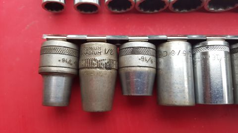 1965 Ford Mustang - A collection of metal sockets, some marked with sizes and 'CHROMIUM VANADIUM', arranged on a red surface.