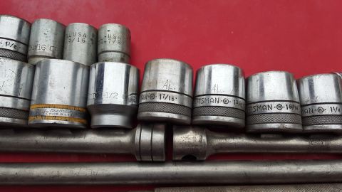 1965 Ford Mustang - A collection of metal sockets and a ratchet are laid out on a red surface, showing different sizes and brands.
