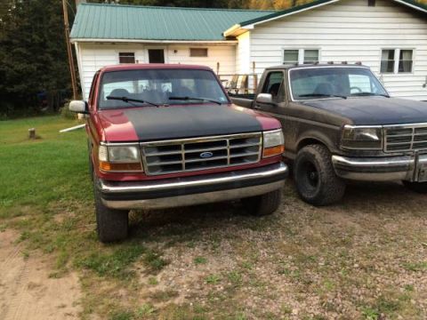 1994 Ford Bronco - Two trucks are parked in a yard in front of a house.