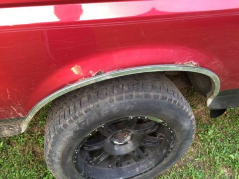 1994 Ford Bronco - Close-up of a red 1994 Ford Bronco's rear fender showing rust damage and a custom wheel.