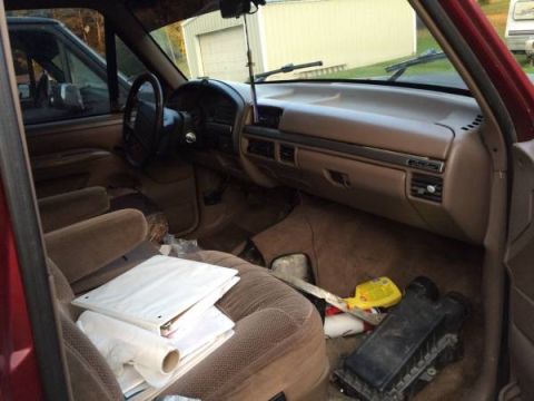 1994 Ford Bronco - The interior of a red SUV is shown, with a view of the dashboard, steering wheel, and seats. Another vehicle is visible through the driver'…