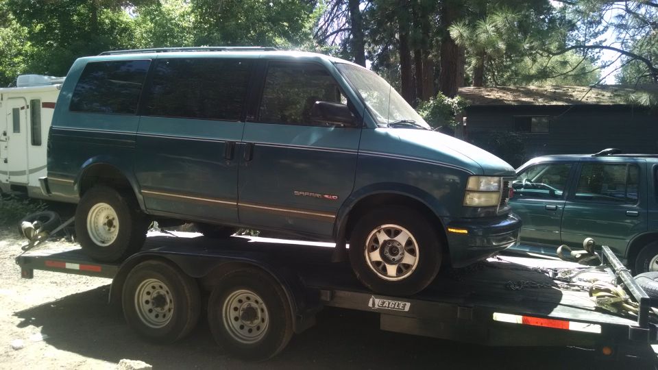 Teal 1995 GMC Safari van on a dual-axle trailer, side view, with another green SUV parked behind it