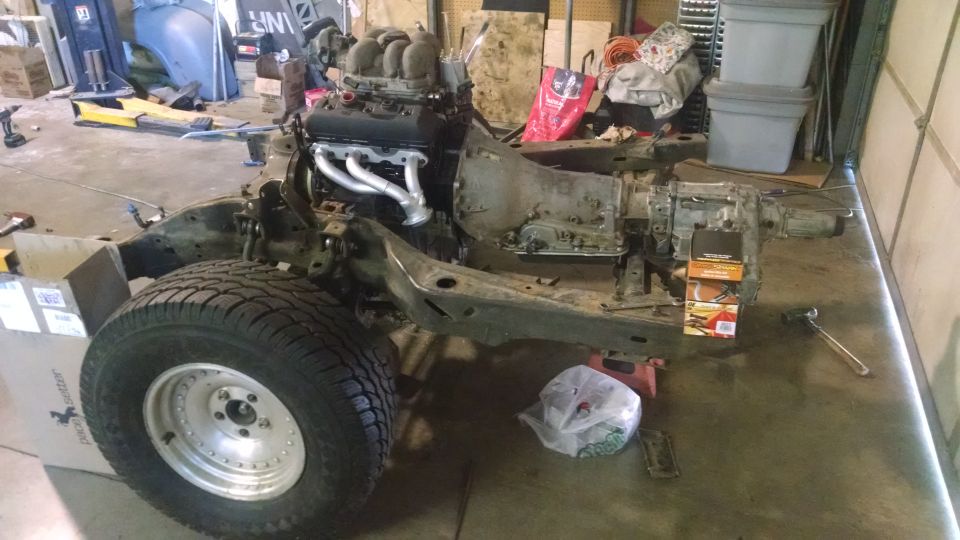 Vehicle chassis with engine and transmission, front tire visible, in a garage