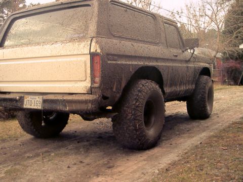 1978 Ford Bronco - This 1978 Ford Bronco is heavily covered in mud, seen from the rear on a dirt road.