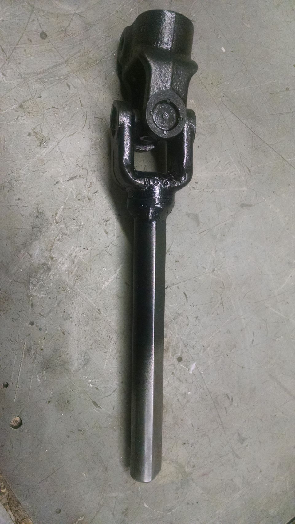 Black metal steering shaft universal joint on a grey concrete surface