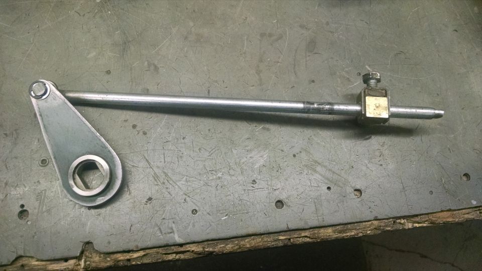Metal linkage with a triangular arm and a bolt on a threaded rod