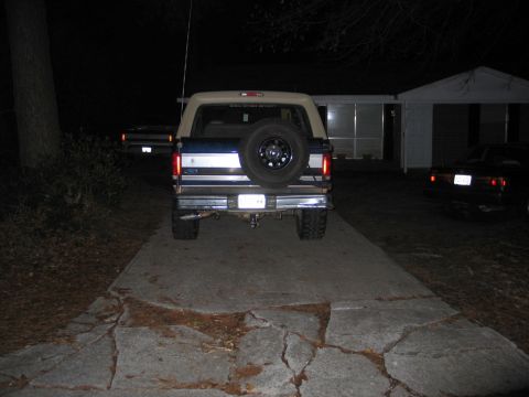1995 Ford Bronco - A blue and tan Ford Bronco is parked on a cracked driveway at night, with another vehicle visible in the background.
