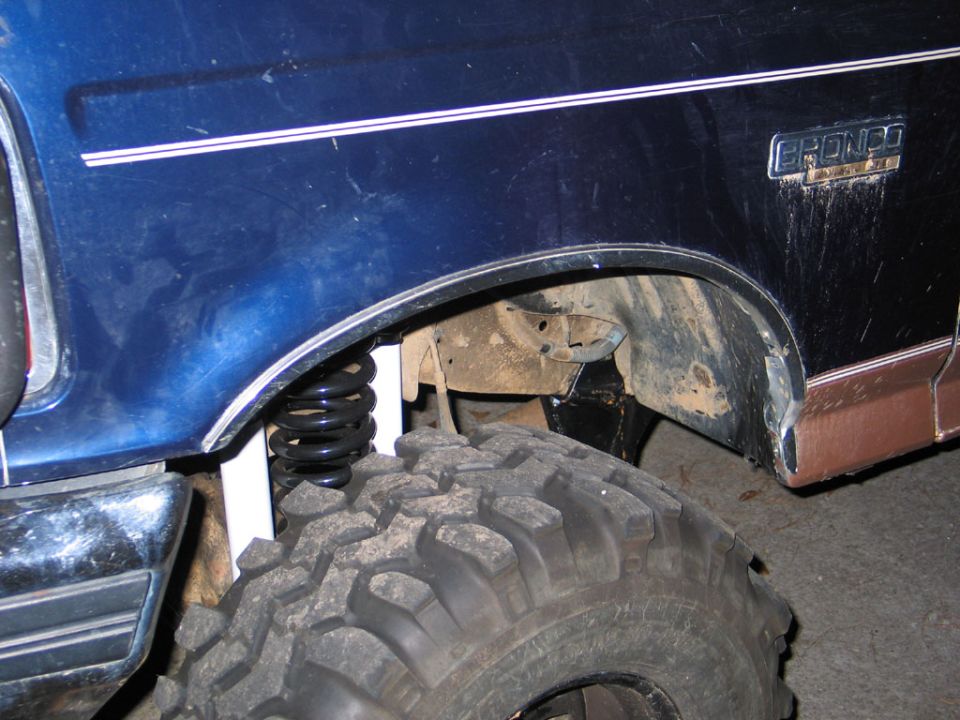 Trimmed front fender of a blue Ford Bronco with coil spring and oversized mud tire
