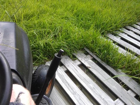 2006 Honda RANCHER - View from the driver's seat of a lawn mower, positioned near overgrown grass and weathered wooden planks.
