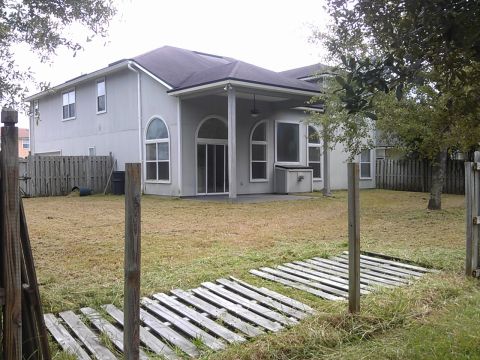 2006 Honda RANCHER - A backyard scene a light gray house with arched windows and a covered patio, bordered by a wooden fence.