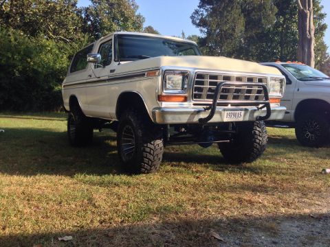 1979 Ford Bronco - Lifted 1979 Ford Bronco with a custom grille guard is parked on grass next to another vehicle.