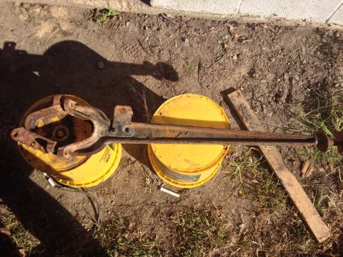 1979 Ford Bronco - A rusty vehicle axle assembly is shown outdoors, supported by two yellow buckets and some wooden planks.