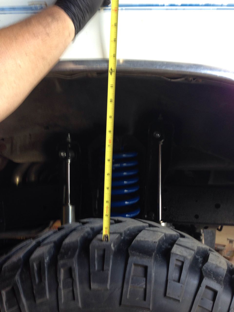 Measuring tire clearance with a yellow tape measure. Blue coil spring visible