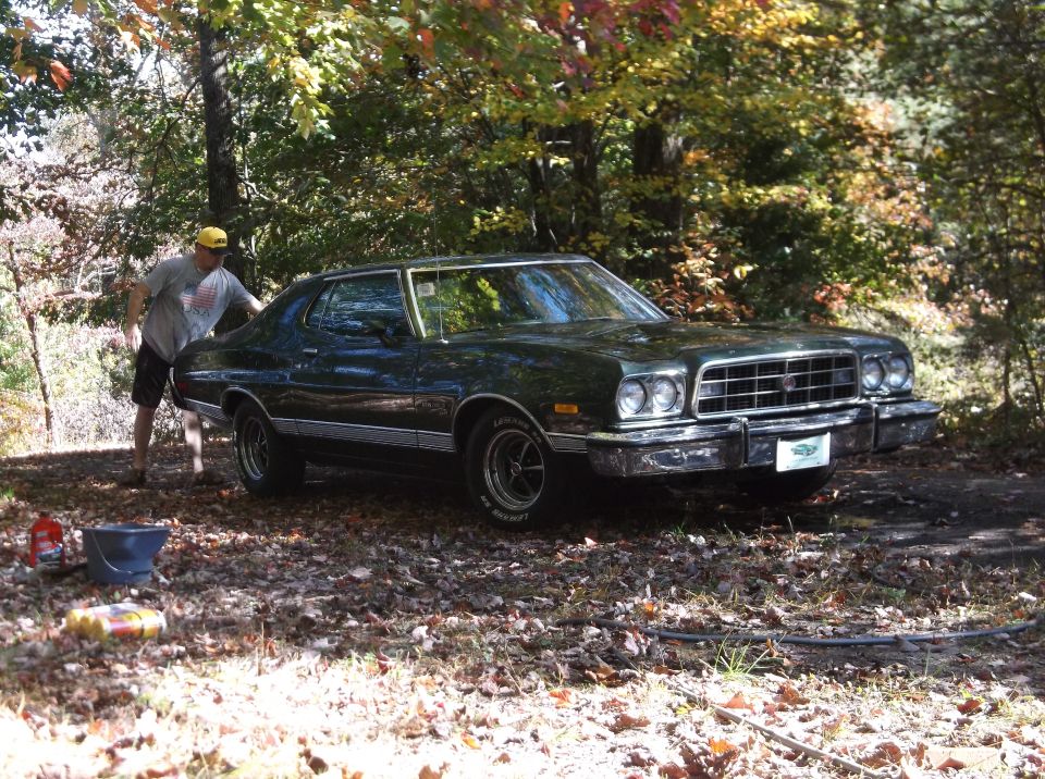 Dark green 1977 Ford Ranchero with chrome grille and bumper, parked outdoors with a person nearby