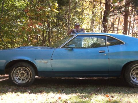 1979 Ford Ranchero - A man leans out the window of a blue 1977 Ford Gran Torino coupe parked outdoors.