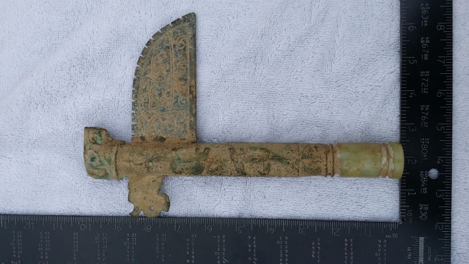 old bronze artifact with intricate carvings, next to a ruler