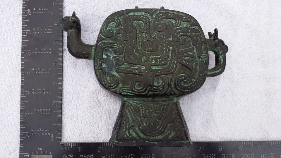 Bronze vessel with animal motifs and intricate carvings, next to a ruler
