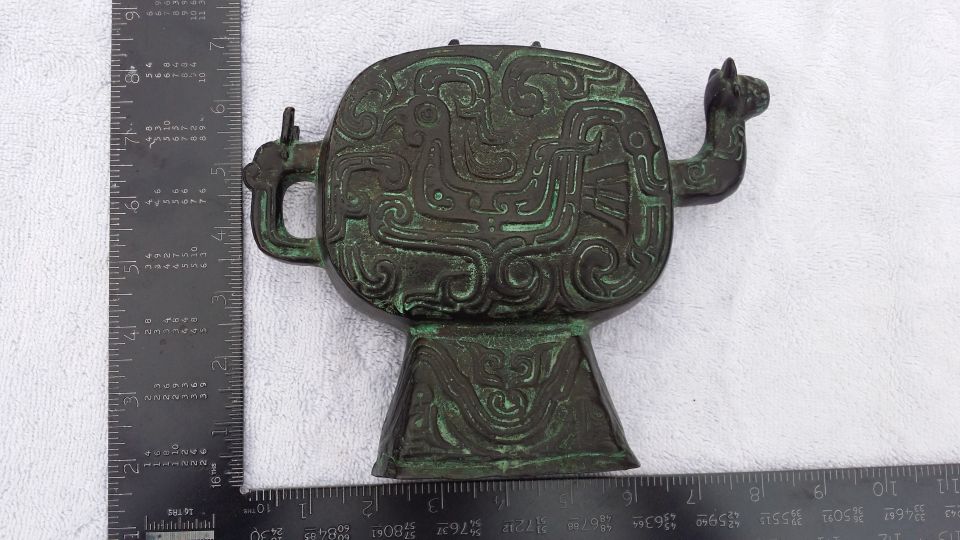 Bronze ritual vessel with intricate carvings and a pedestal base, measured against rulers