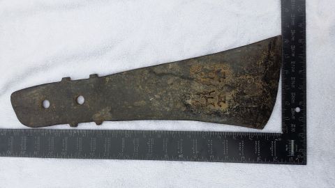 2007 Subaru Impreza - A close-up view of a heavily rusted metal component, two circular holes and embossed markings, placed alongside measuring rulers for scale.