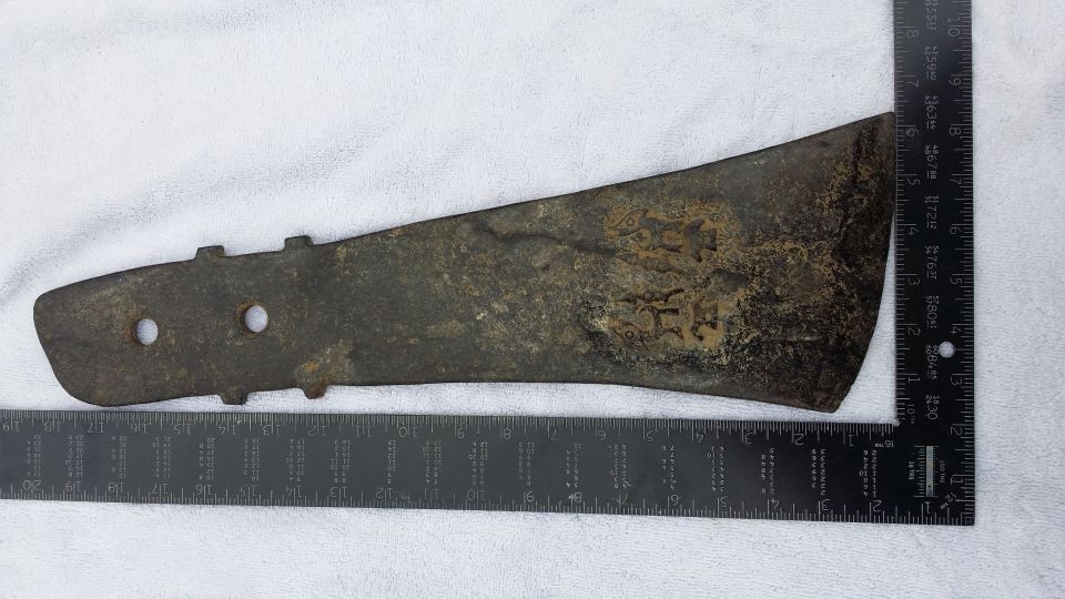 Rusted metal part with two holes and embossed markings, measured against rulers