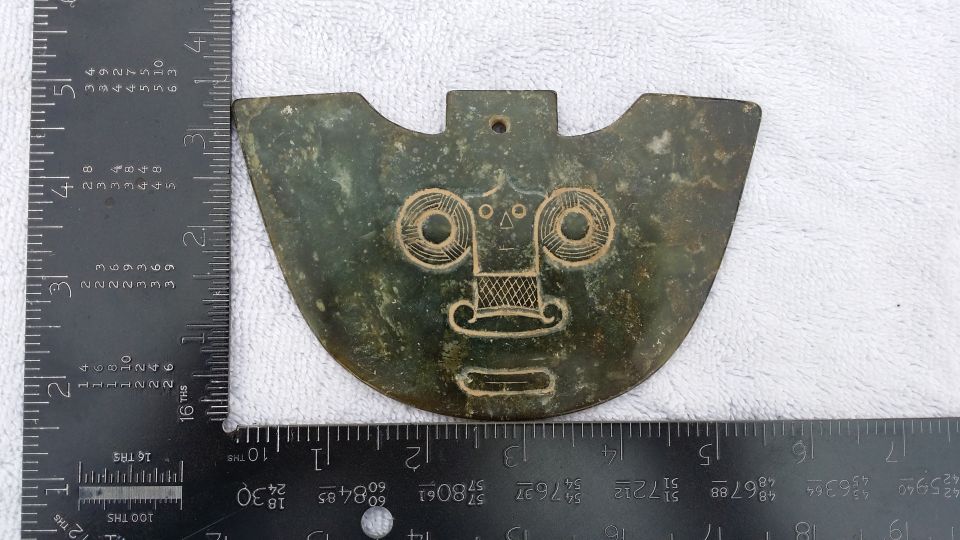 Green jade pendant with carved face, measured by rulers