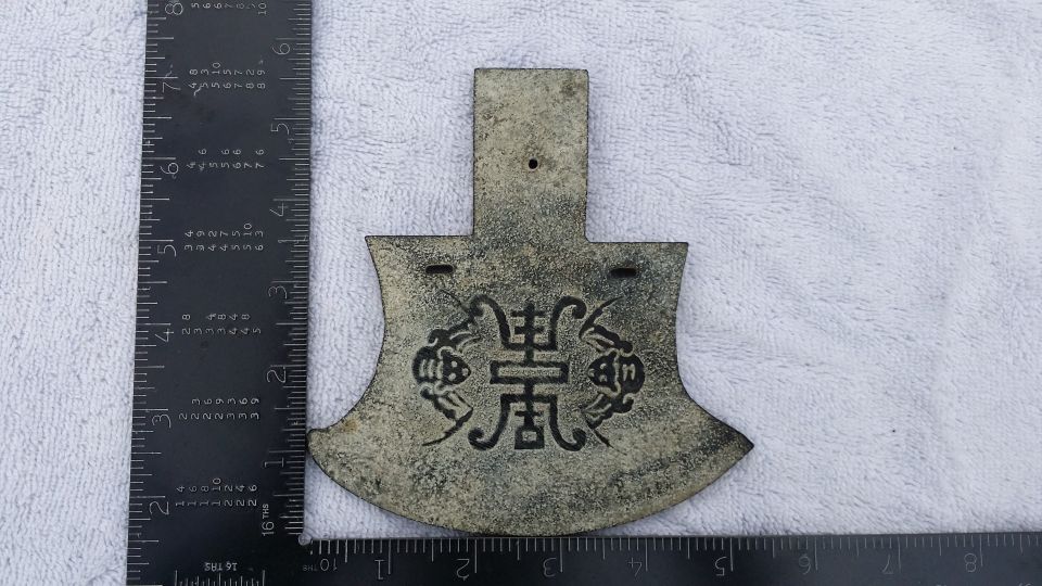 Old bronze coin with Chinese characters and designs, next to a ruler