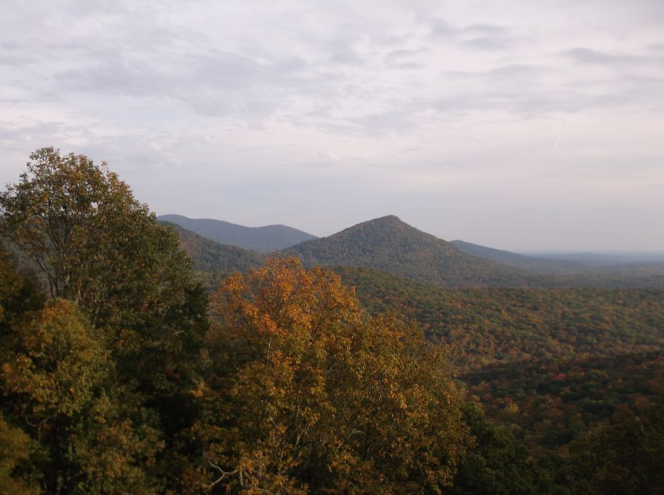Mountain range with trees in autumn colors under a cloudy sky. A watermark reads SUPERMOTORS