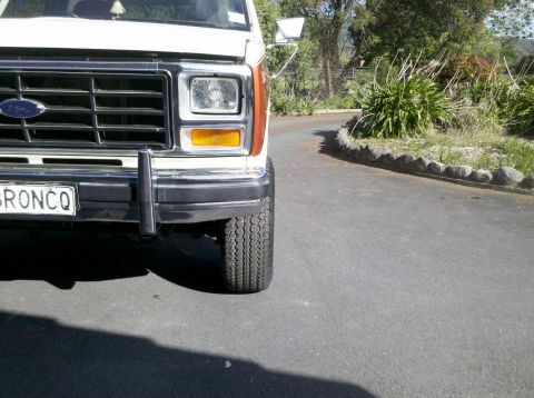 1982 Ford Bronco - The front grille and headlights of a white Ford Bronco are visible, parked on an asphalt driveway.