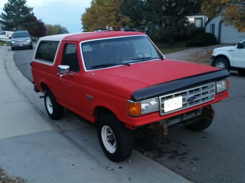 1988 Ford Bronco - A red Ford Bronco with a white top is parked on a residential street.