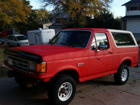 1988 Ford Bronco - This red Ford Bronco is parked in a driveway on a sunny day, with trees and houses visible.
