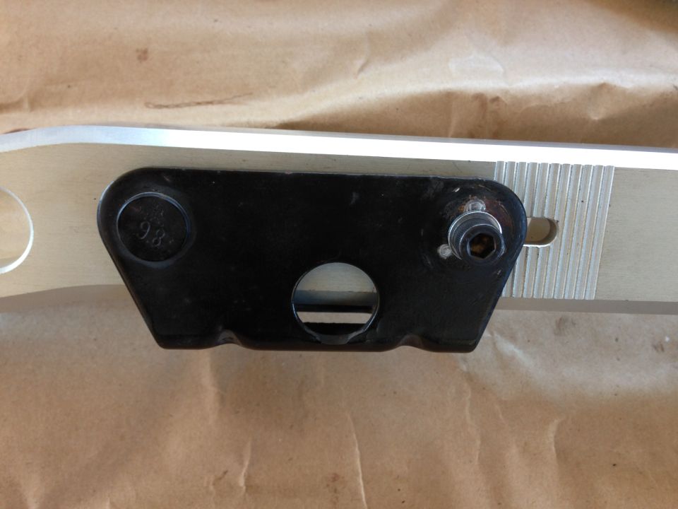 Black metal bracket with a bolt and a circular hole, mounted on a silver piece with ribbed texture. Text '9.8' is visible on the bracket