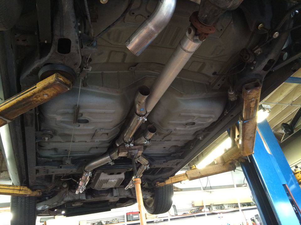 Underside of a car on a lift showing a custom dual exhaust system with new pipes and mufflers
