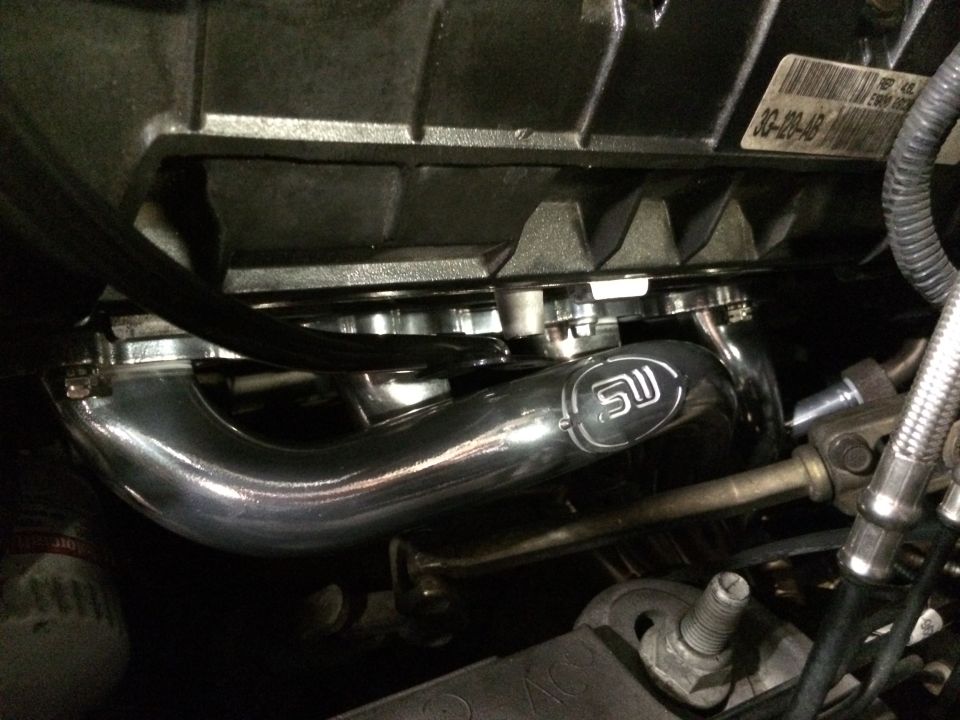 Chrome exhaust manifold with SW logo attached to engine block