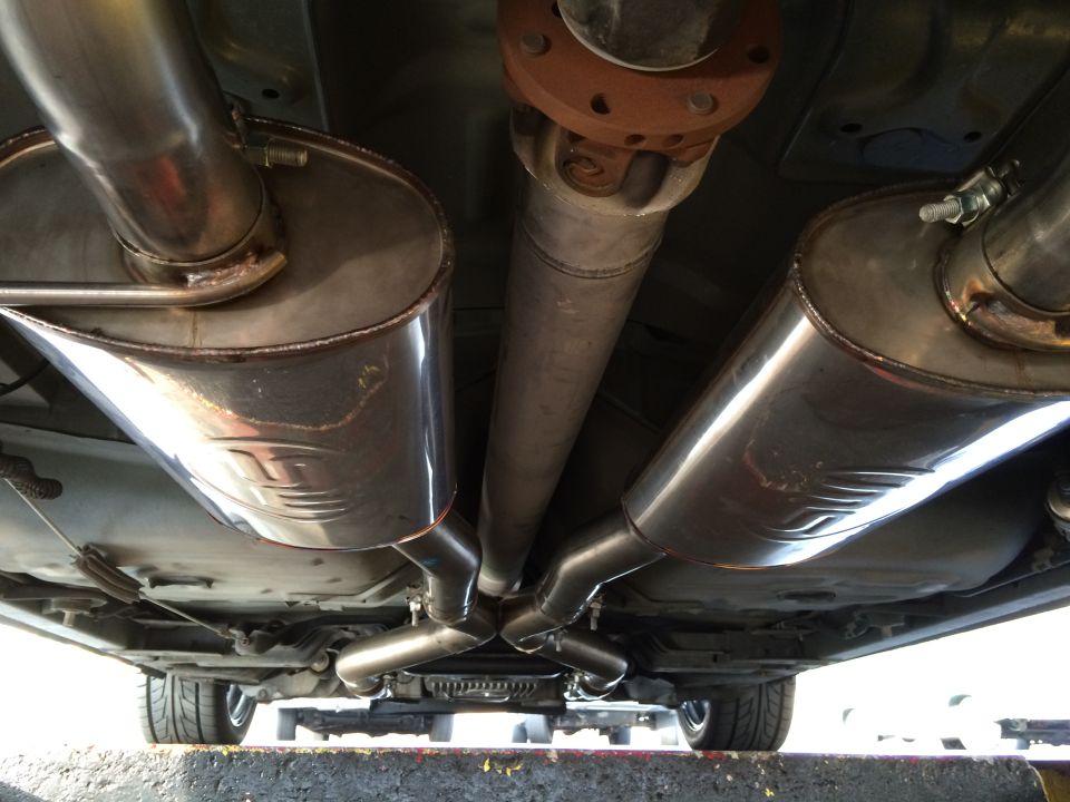 Underside view of a car's dual exhaust system with polished mufflers and a driveshaft