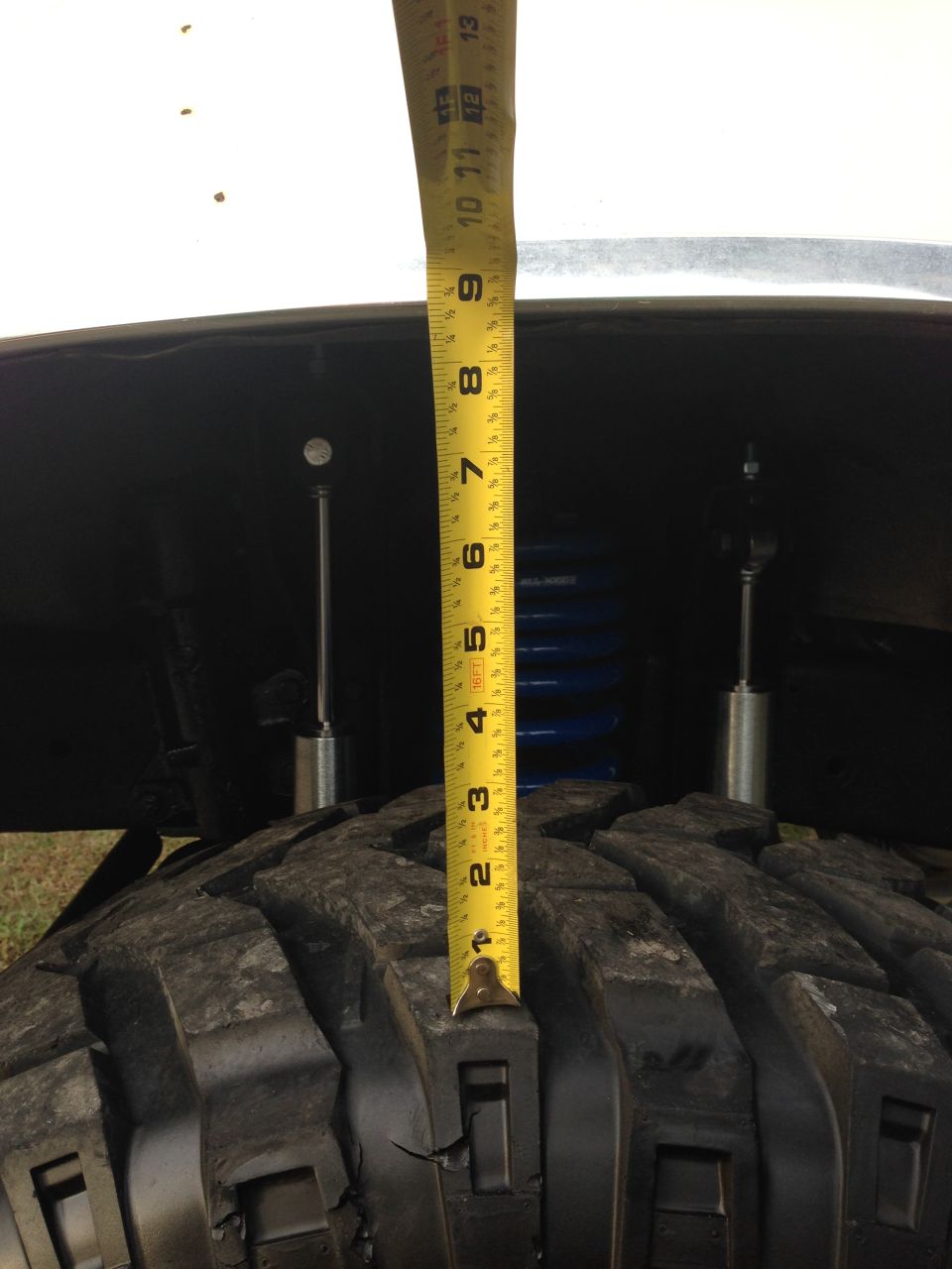 Measuring suspension lift on a vehicle with a tape measure. Shows tire, shock, and blue coil spring