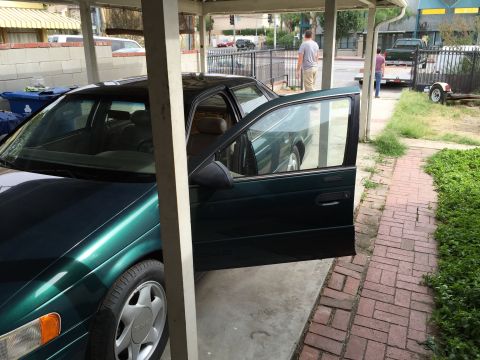 1993 Ford Taurus - Green sedan parked under a carport, driver's door ajar. The vehicle's body style suggests a mid-1990s model year.