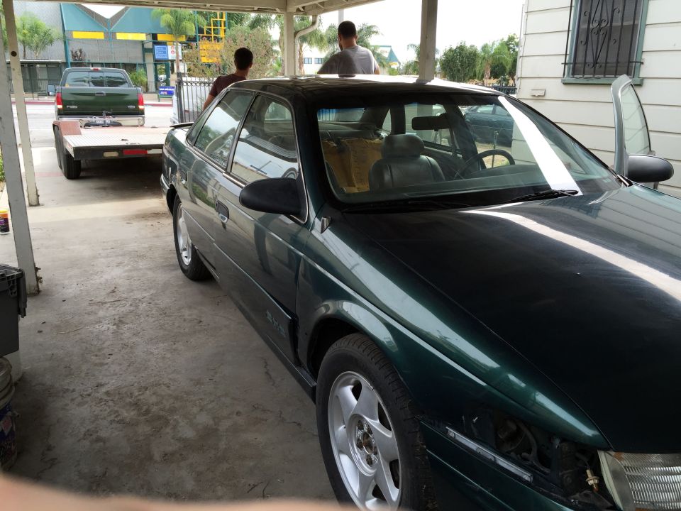1993 Ford Taurus, dark green, parked under a carport with a trailer and pickup truck in the background
