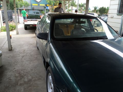 1993 Ford Taurus - A dark green sedan is parked under a carport, with a pickup truck on a trailer in the background.