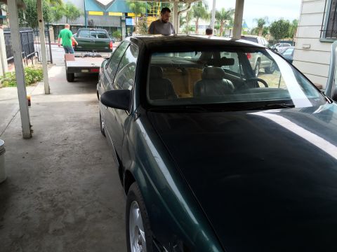 1993 Ford Taurus - A dark green 1993 Ford Taurus sedan is parked under a carport, with a trailer and pickup truck visible in the background.