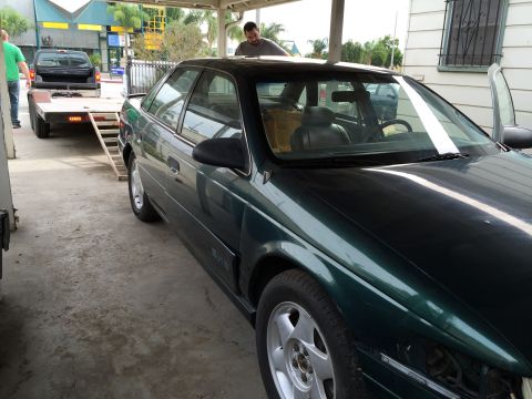 1993 Ford Taurus - A 1993 Ford Taurus is parked under a carport, with a pickup truck and trailer in the background.